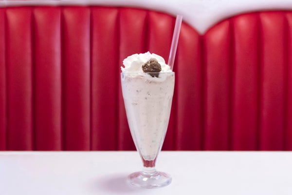 Milkshake with whipped cream and a cherry in a glass, placed on a table in front of a red upholstered booth
